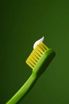 Green plastic toothbrush with white toothpaste on a green background. Foto stock