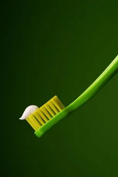 Green plastic toothbrush with white toothpaste on a green background. Stock Photos