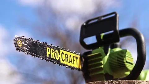 Green Pro Craft cordless chainsaw standing on a wooden stump Stock Footage 332875005
