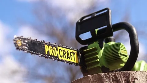 Green Pro Craft cordless chainsaw standing on a wooden stump Stock Footage 332875008