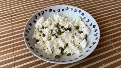 Green pumpkin seeds fall into cottage cheese on a white plate for healthy eating Stock Footage 300052203
