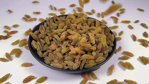 Green raisins falling in dark plate, white background, slow motion Stock Footage 336847942