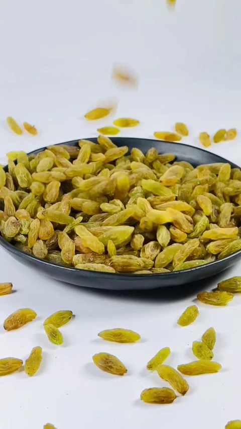 Green raisins falling in dark plate, white background, slow motion Stock Footage 336847943
