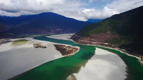 Green river bend and sandbar island beneath low mountain clouds in Tibet Video stock 345881098