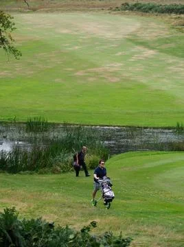 A green rolling golf course with two golfers near a lake Stock Photos