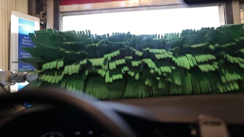 Green round brush rotates in front of the windshield of the car at the car wash Stock Footage 129709163