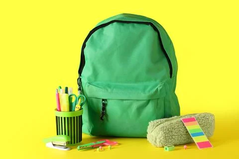 Green school backpack and different stationery on yellow background Stock Photos