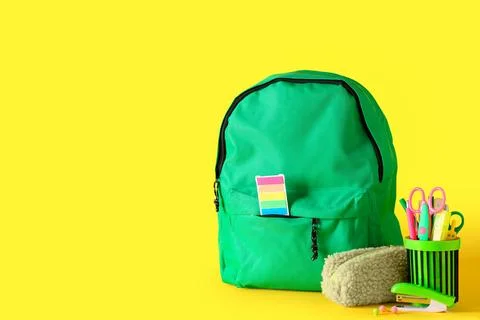 Green school backpack and different stationery on yellow background Stock Photos