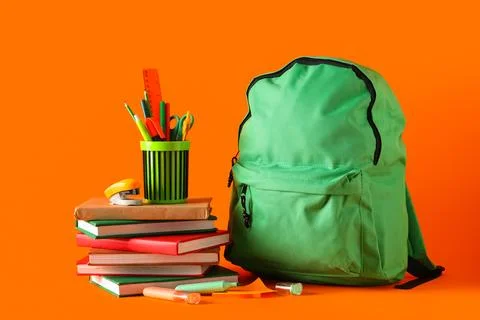 Green school backpack with different stationery on orange background Stock Photos