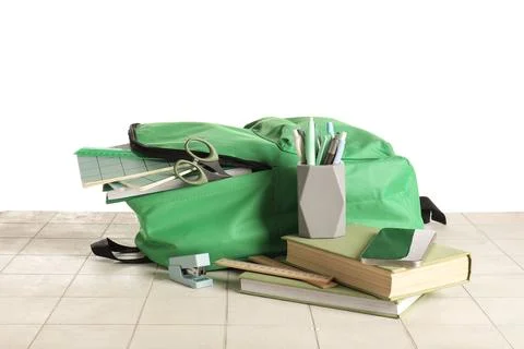 Green school backpack with different stationery supplies on tile table agains Stock Photos