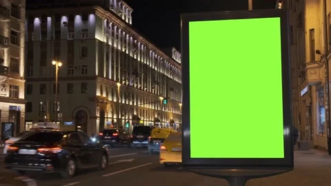 A green screen billboard located on the sidewalk on which people walk, next to a Vidéo 142084948