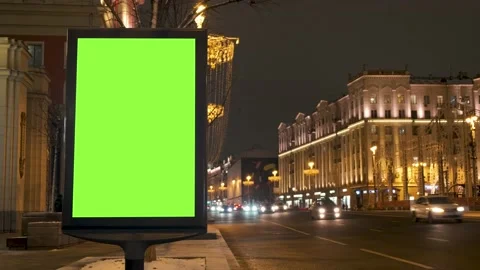 A green screen billboard located on the sidewalk on which people walk, next to a Stock Footage 148311739