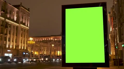 A green screen billboard located on the sidewalk on which people walk, next to a Stock Footage 154865978