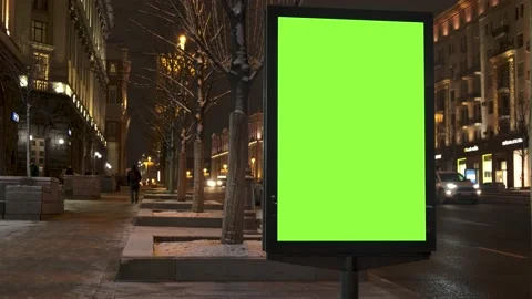 A green screen billboard located on the sidewalk on which people walk, next to a Stock Footage 154865996