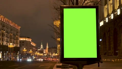 A green screen billboard located on the sidewalk on which people walk, next to a Stock Footage 154866320