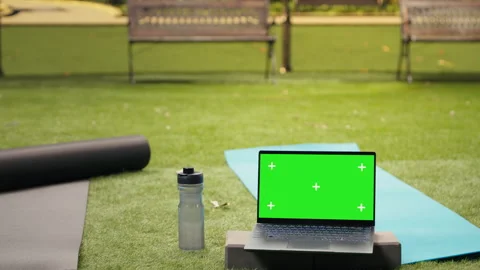 Green screen chroma key on laptop close to yoga mat on grass in public park Stock Footage 346020958