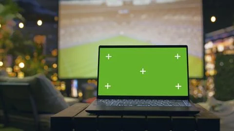 Green screen laptop in cozy rooftop lounge with football match projection Stock Photos