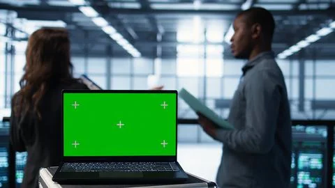 Green screen laptop in front of data center engineers inspecting servers 스톡 사진