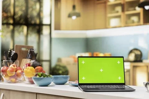 Green screen on a laptop placed on empty table in modern kitchen space Foto stock
