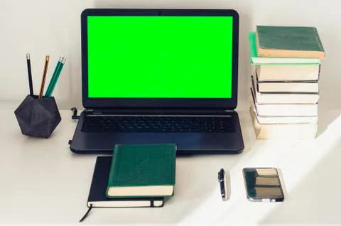 Green screen laptop, stack of books, notebook and pencils on white table, edu Stock Photos