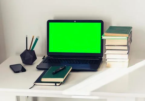 Green screen laptop, stack of books, notebook and pencils on white table, edu Stock Photos