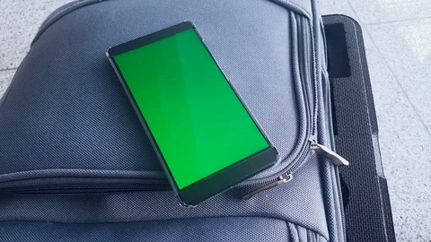 Green screen on mobile phone placed on a suitcase in an airport Stock Footage 98108944