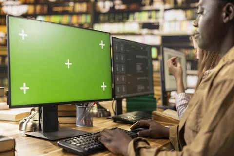 Green screen mockup on computer desktop near student at shared library table 写真素材