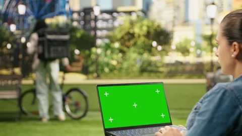 Green screen mockup display on laptop held by woman in green urban park Stock Footage 343500761