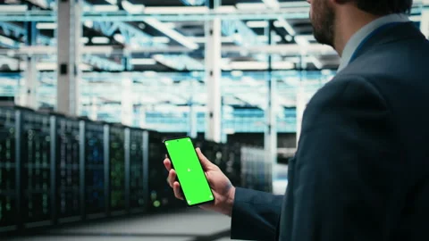 Green screen smartphone used by data center admin managing wireframe mesh gear Stock Footage 329530560