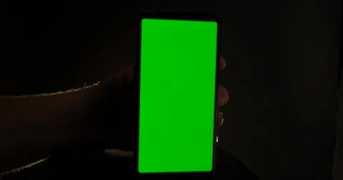 Green screen on smartphone vertical view man holding back lit isolated on black Stock Footage 205489311