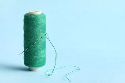 Green sewing thread with needle on blue background Stock Photos