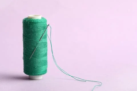 Green sewing thread with needle on lilac background Stock Photos