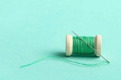 Green sewing thread with needle on turquoise background Stock Photos