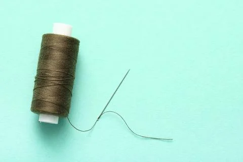 Green sewing thread with needle on turquoise background Stock Photos