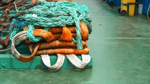 Green ship deck featuring stacked orange lifting slings and coiled green rope Stock Photos