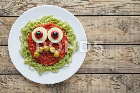Green spaghetti pasta creative spooky halloween food monster with sad smile Stock Photos