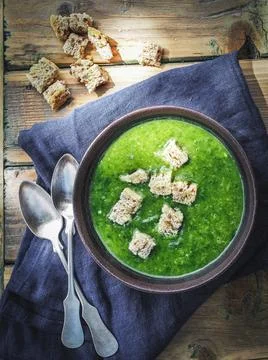 Green spinach soup with piece of bread in brown bowl. Stock Photos