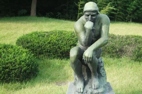 Green statue of thinker Auguste Rodin, setting naked on a rock Stock Photos