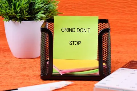 A green sticky note with black text sits in a holder, displaying grind do n.. Stock Photos