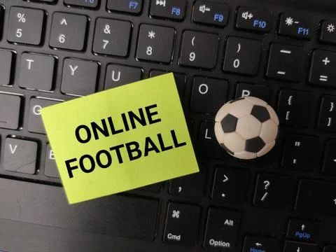 A green sticky note with the text ONLINE FOOTBALL sits on a black keyboard .. Stock Photos