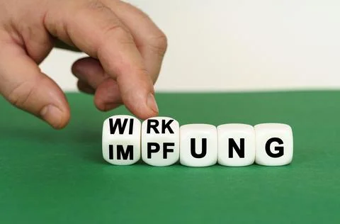 On a green surface are white cubes with the inscription - WIRKUNG or IMPFUNG Stock Photos