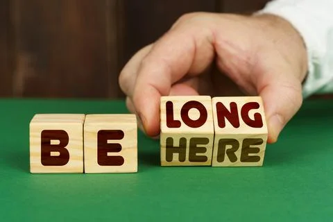 On a green surface, a man puts cubes with the inscription - BELONG, BEHERE 스톡 사진