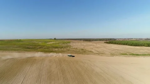 A green SUV drives quickly along a dirt road between two fields. Video stock 235528554