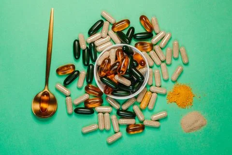 Green tabletop with an array of vitamin supplement capsules and pills and a spoo Stock Photos