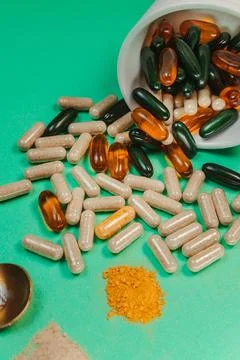 Green tabletop with an array of vitamin supplement capsules and pills and a spoo Stock Photos