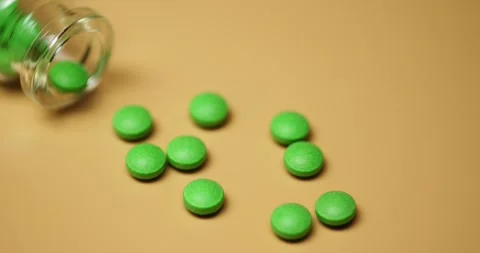 Green tablets spilling out of open bottle on to surface Stock Footage 303056953