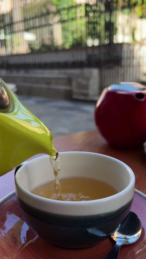 Green tea being poured in a cup from a teapot on terrace of cafe. Vertical video Stock Footage 240919622