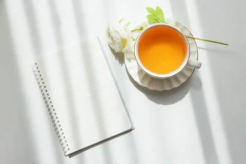 Green Tea Cup with Notebook and Ranunculus Flowers on White Table Foto stock