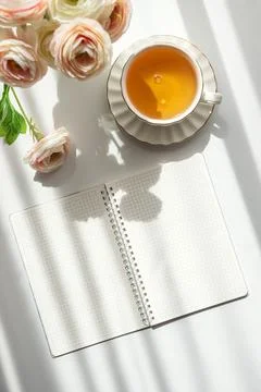 Green Tea Cup with Notebook and Ranunculus Flowers on White Table Foto stock