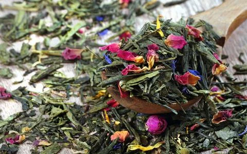 Green tea leaves and dried rose flowers in a wooden spoon. Stock Photos
